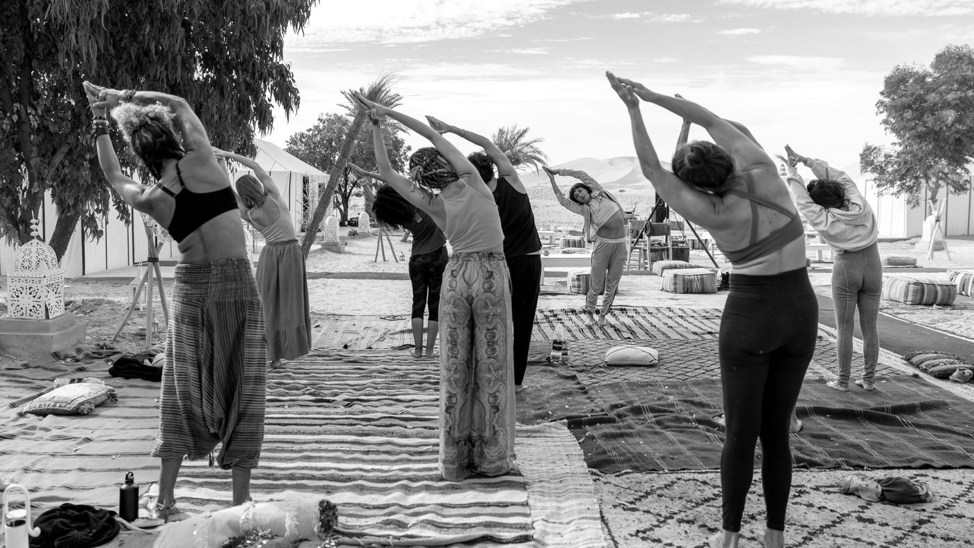 A group stretching together on rugs in the desert, black and white