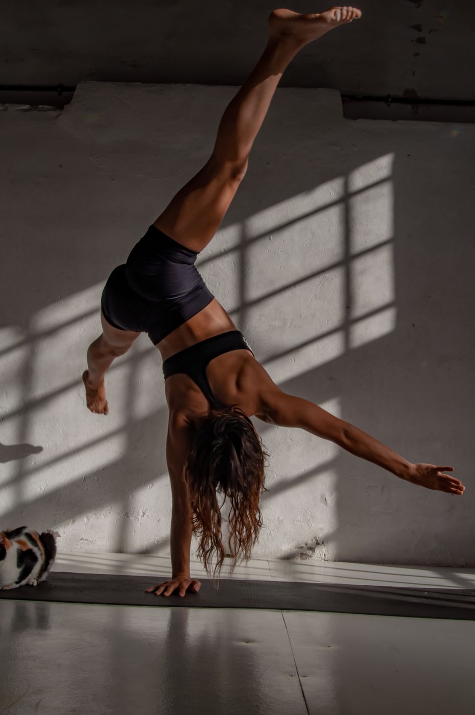 Anita in a one-arm handstand against a sunlit wall